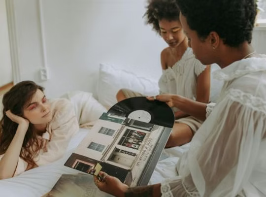 Drei Personen auf einem Bett schauen sich gemeinsam eine Vinyl-Schallplatte an.